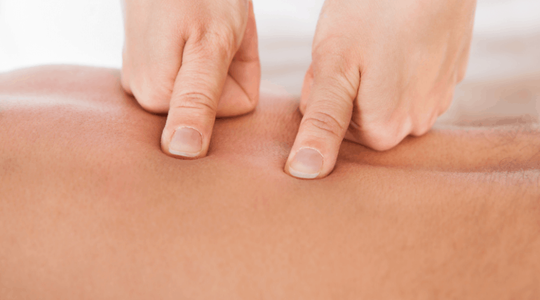 Massage therapist pressing her thumbs into the muscles of her client's back