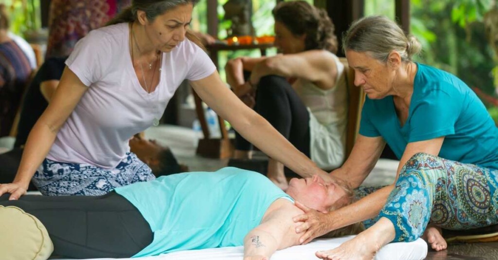 A photo of two women facilitating a breathwork exercise with a woman lying on a mat.
