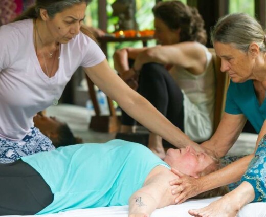 A photo of two women facilitating a breathwork exercise with a woman lying on a mat.