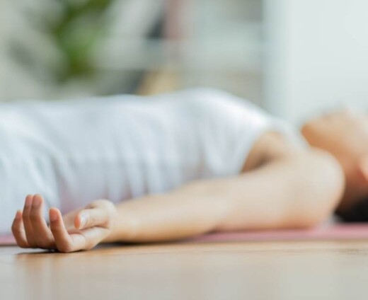 Photo of a woman lying on a yoga mat with hands relaxed outstretched to her sides.