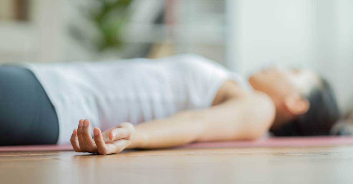 Photo of a woman lying on a yoga mat with hands relaxed outstretched to her sides.