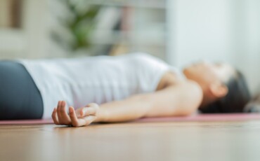Photo of a woman lying on a yoga mat with hands relaxed outstretched to her sides.