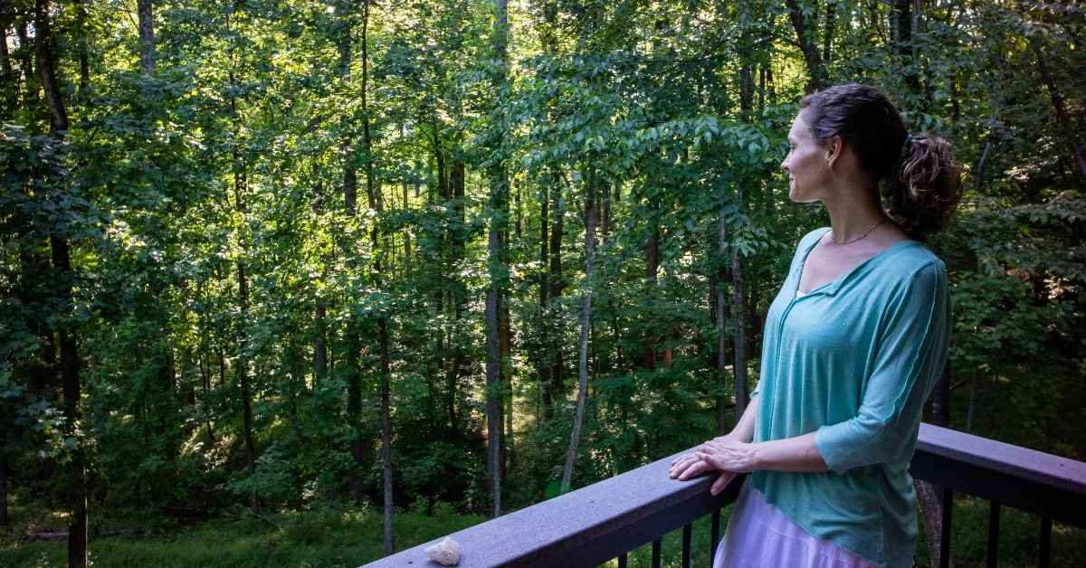 Photo of a young woman gazing into the forest from a deck at The Sanctuary.