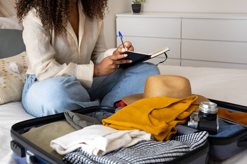woman-writing-in-journal-with-open-suitcase-full-of-clothes-camera-hat